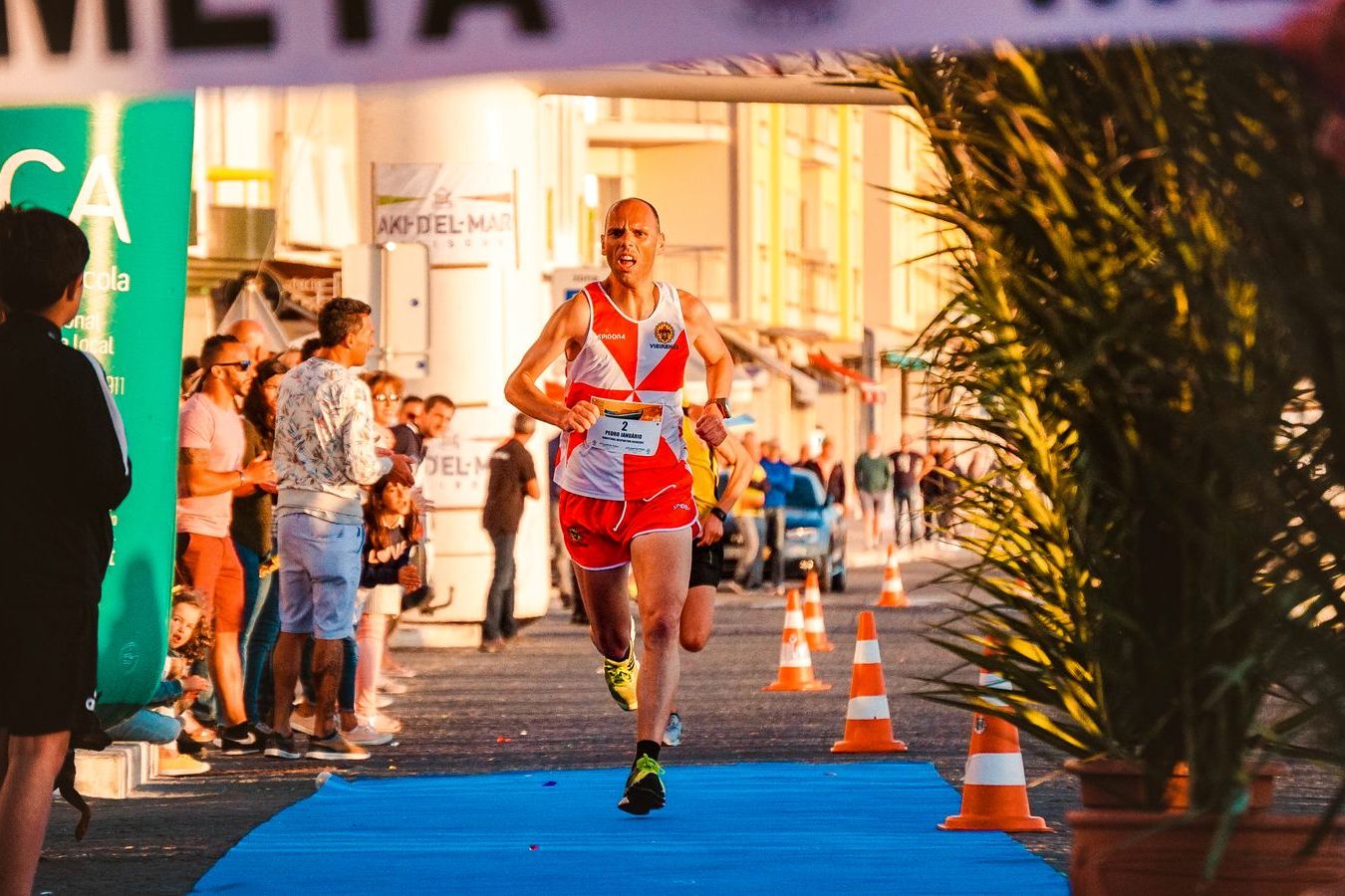 A runner crossing a marathon finish line alone in front of a cheering crowd