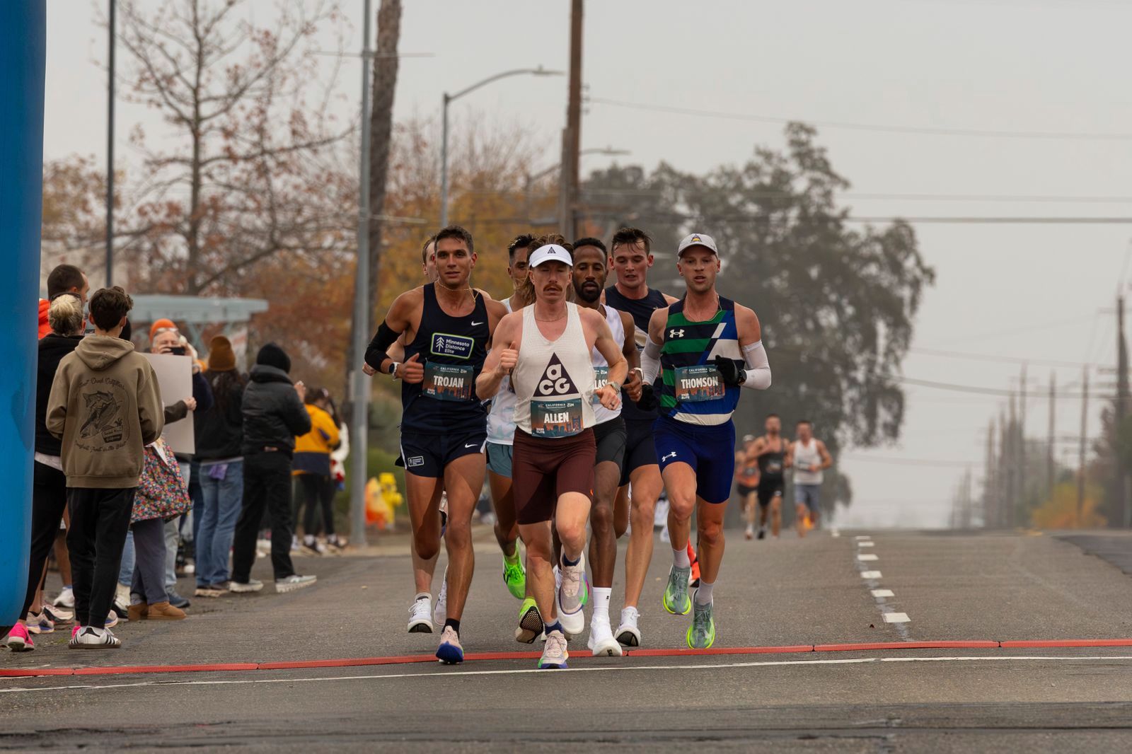 The lead pack of a city marathon running shoulder to shoulder on an overcast day