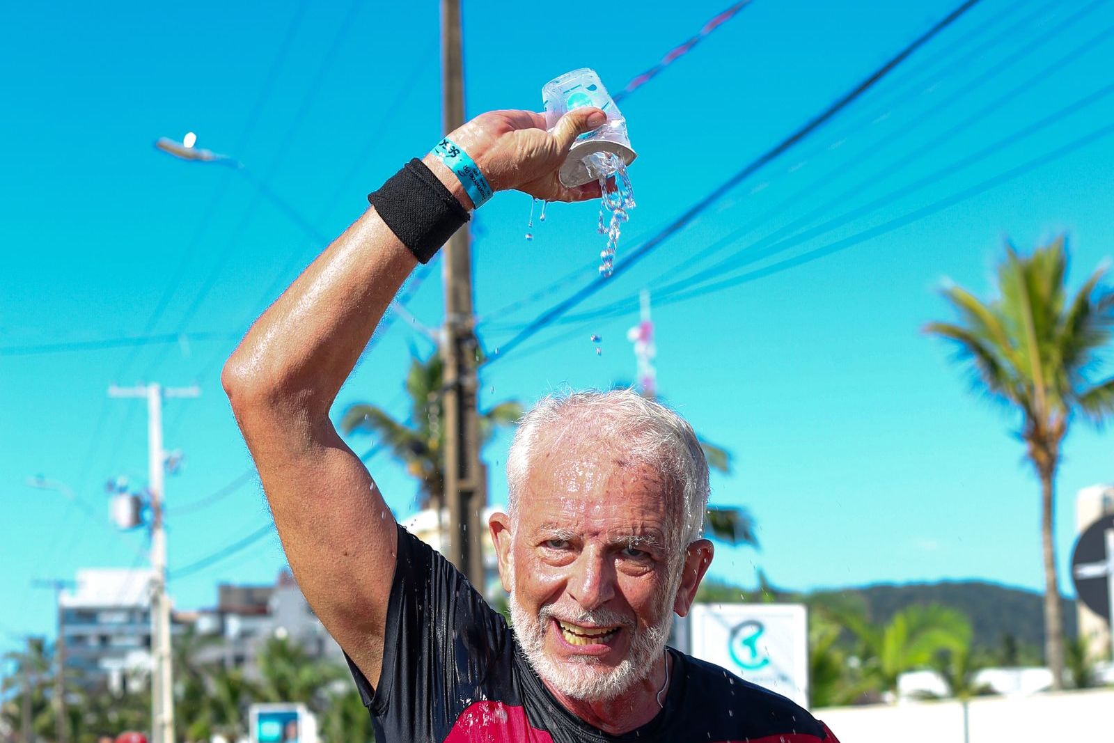 Older marathon runner pouring a cup of water over his head at an aid station in bright sun