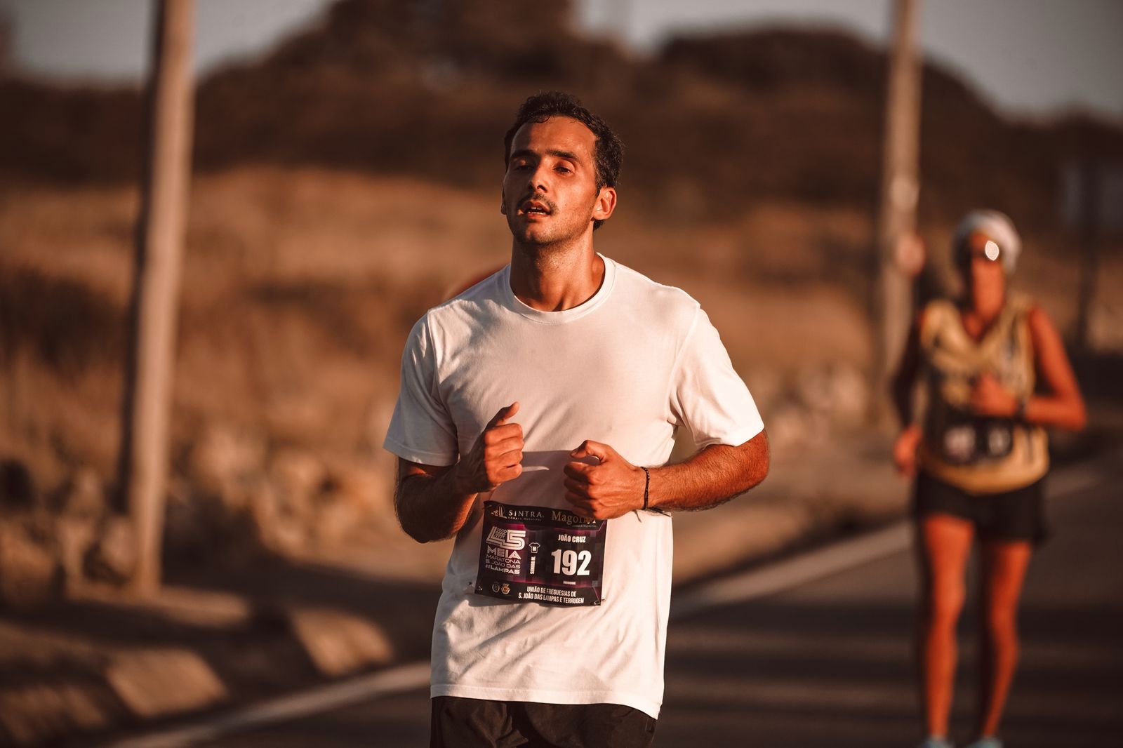 Runner in a white shirt racing in warm late day sunlight, eyes closed
