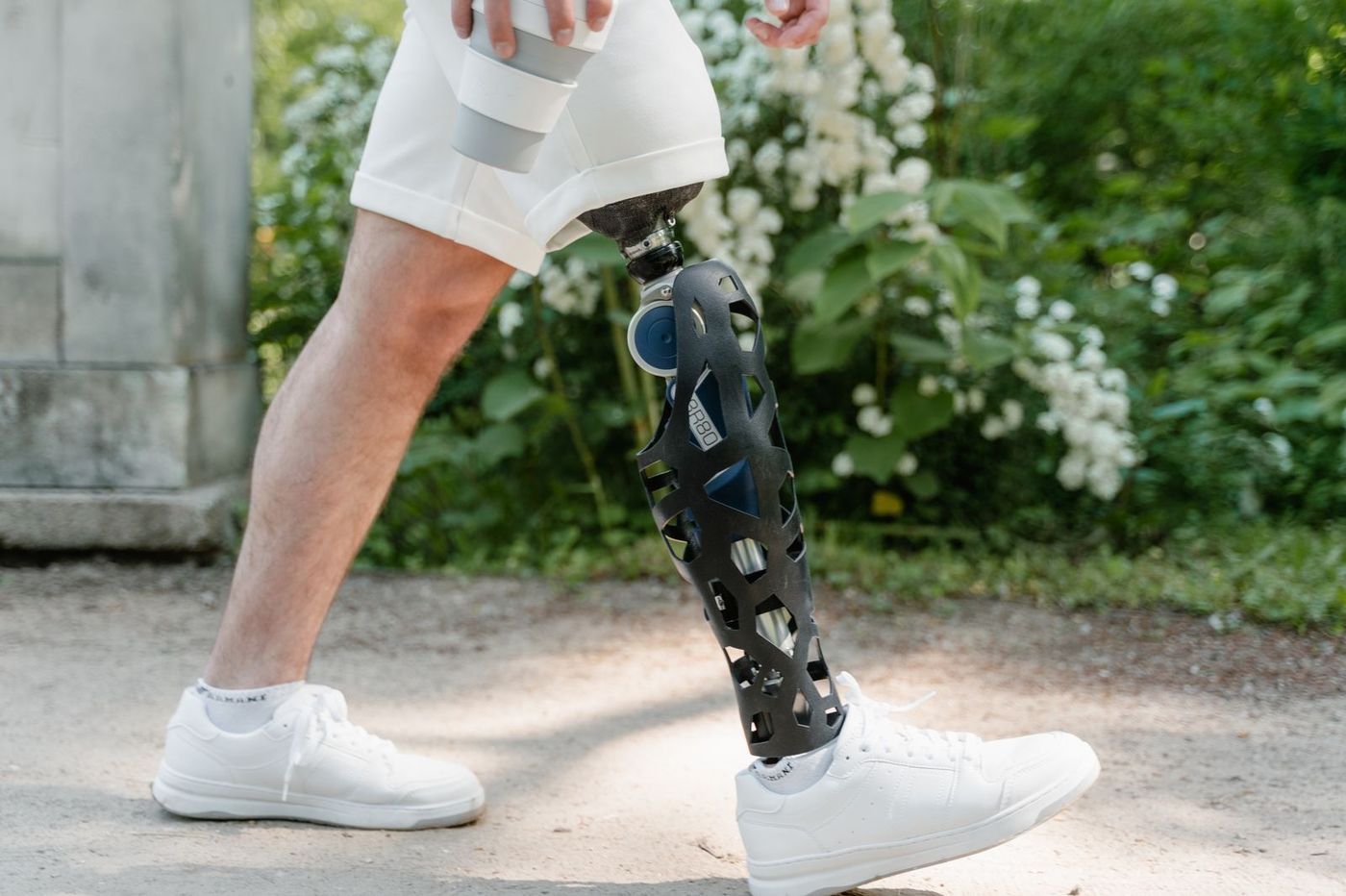 Close up of a man walking outdoors with a prosthetic lower leg, holding a coffee cup