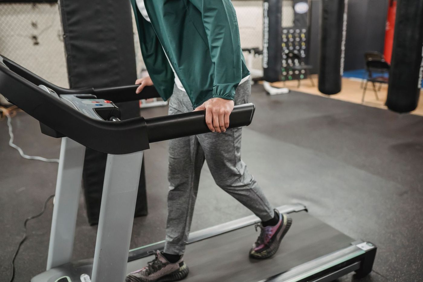 A person walking on a treadmill in a gym, hands resting on the side rails