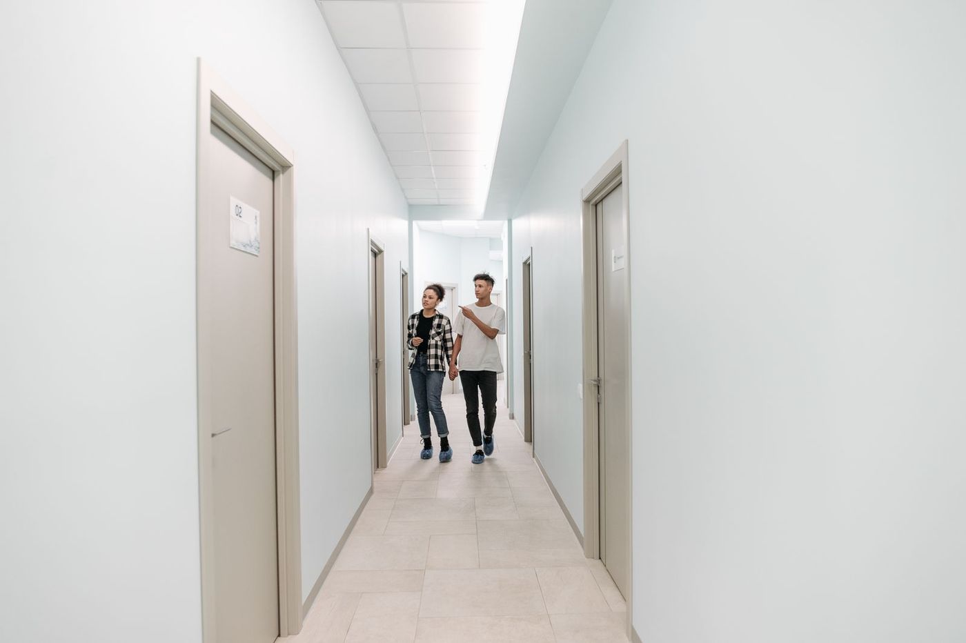 Two people walking toward the camera down a bright clinic corridor lined with doors