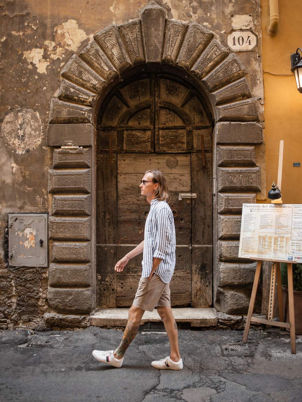 Side view of a man mid stride walking past an old stone doorway