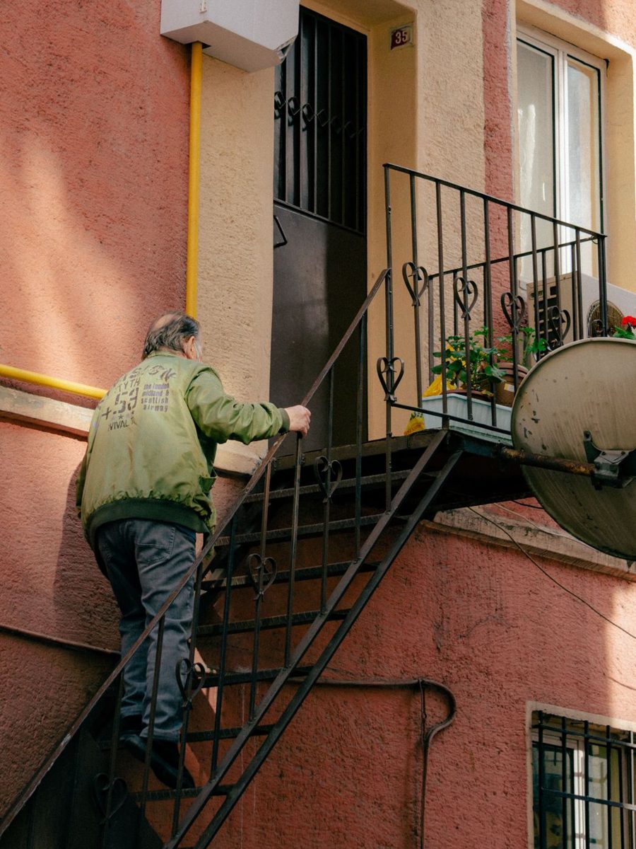 An older man climbing the exterior stairs to his house, one hand on the rail