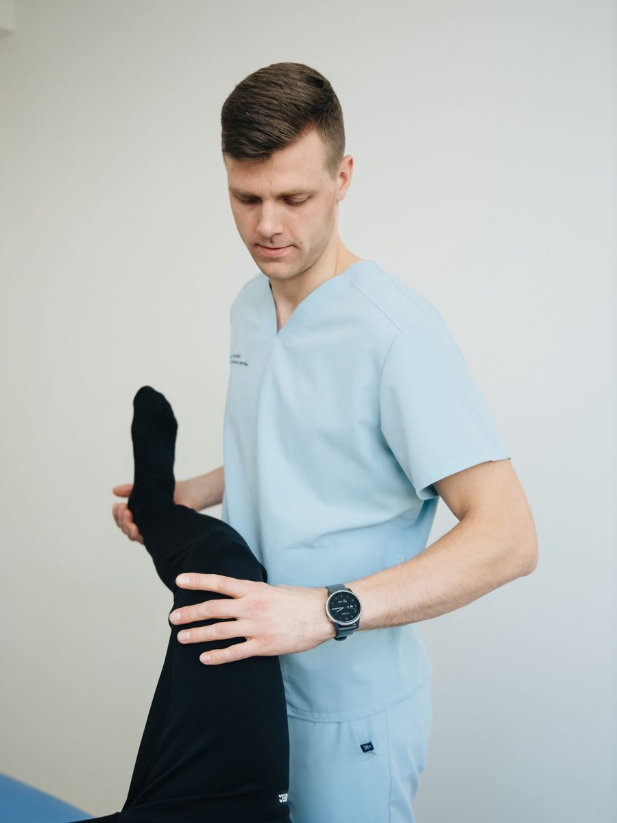 A physiotherapist in scrubs guiding a patient through leg exercises on a treatment table