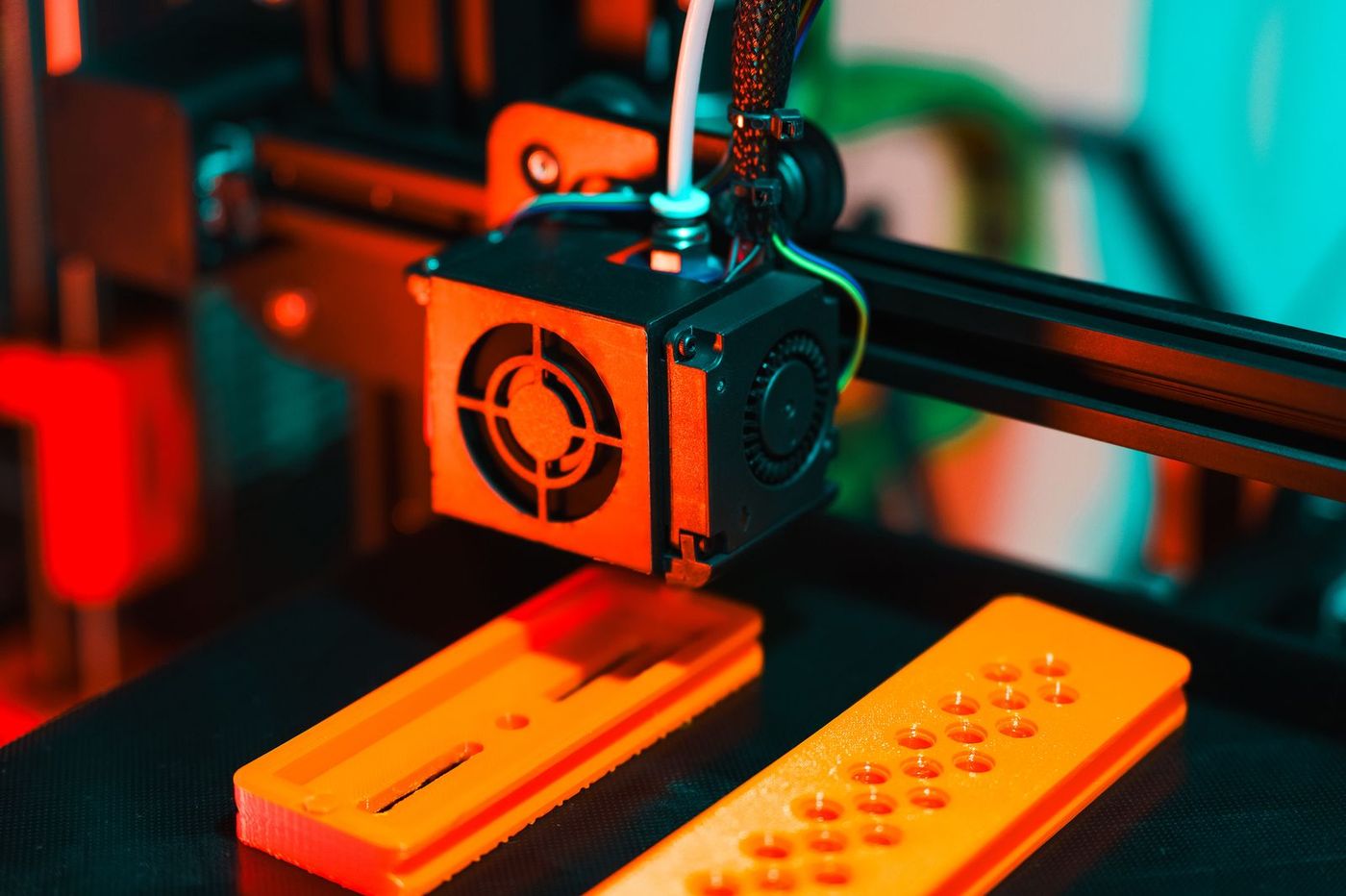 Close up of a 3D printer print head over orange printed parts on the print bed