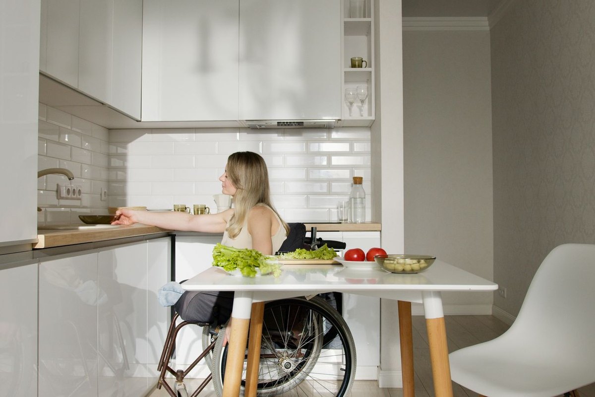 A woman using a wheelchair reaches toward a pan while cooking in her kitchen at home