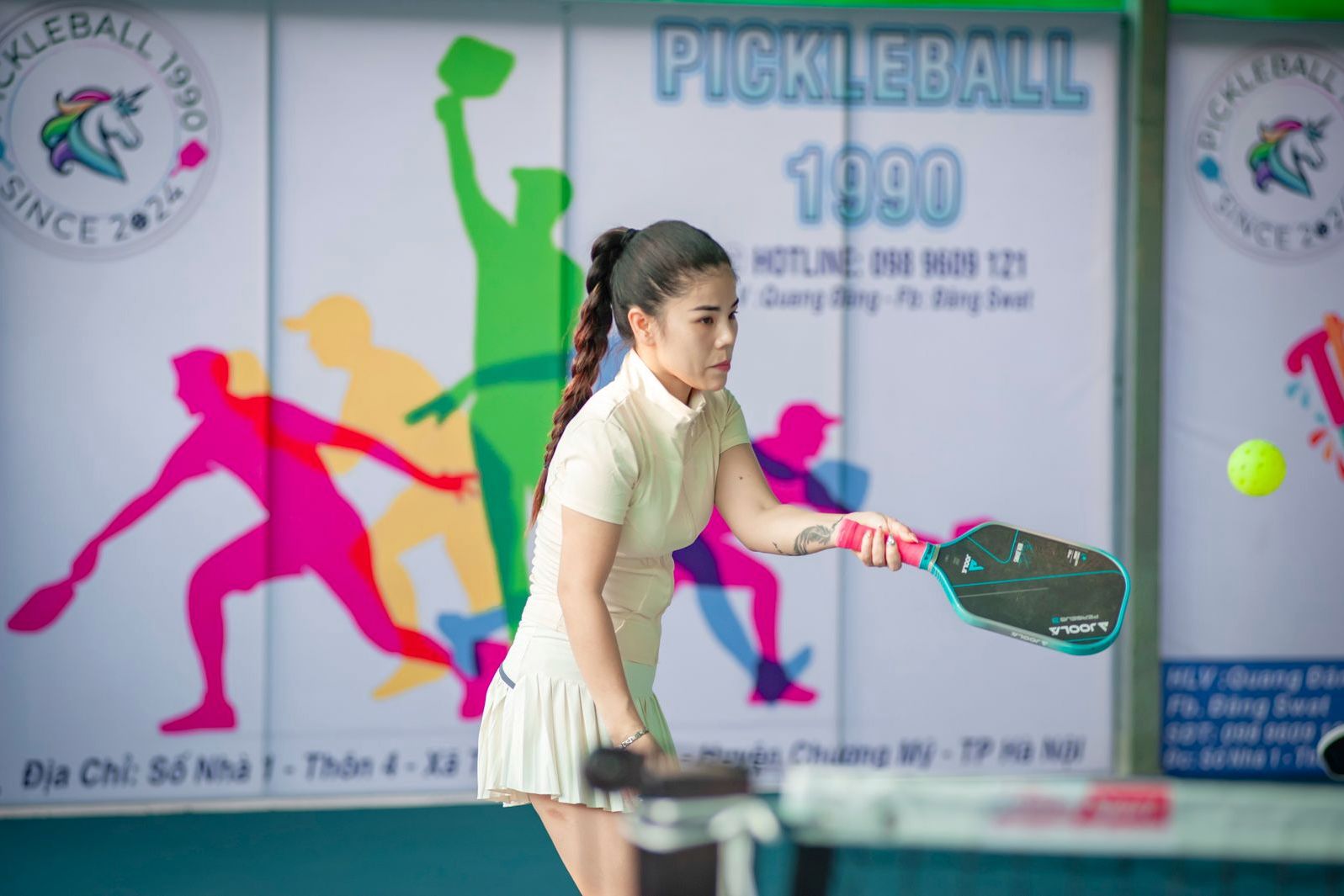 Woman playing pickleball at the net during an indoor match, paddle raised and ball in the air