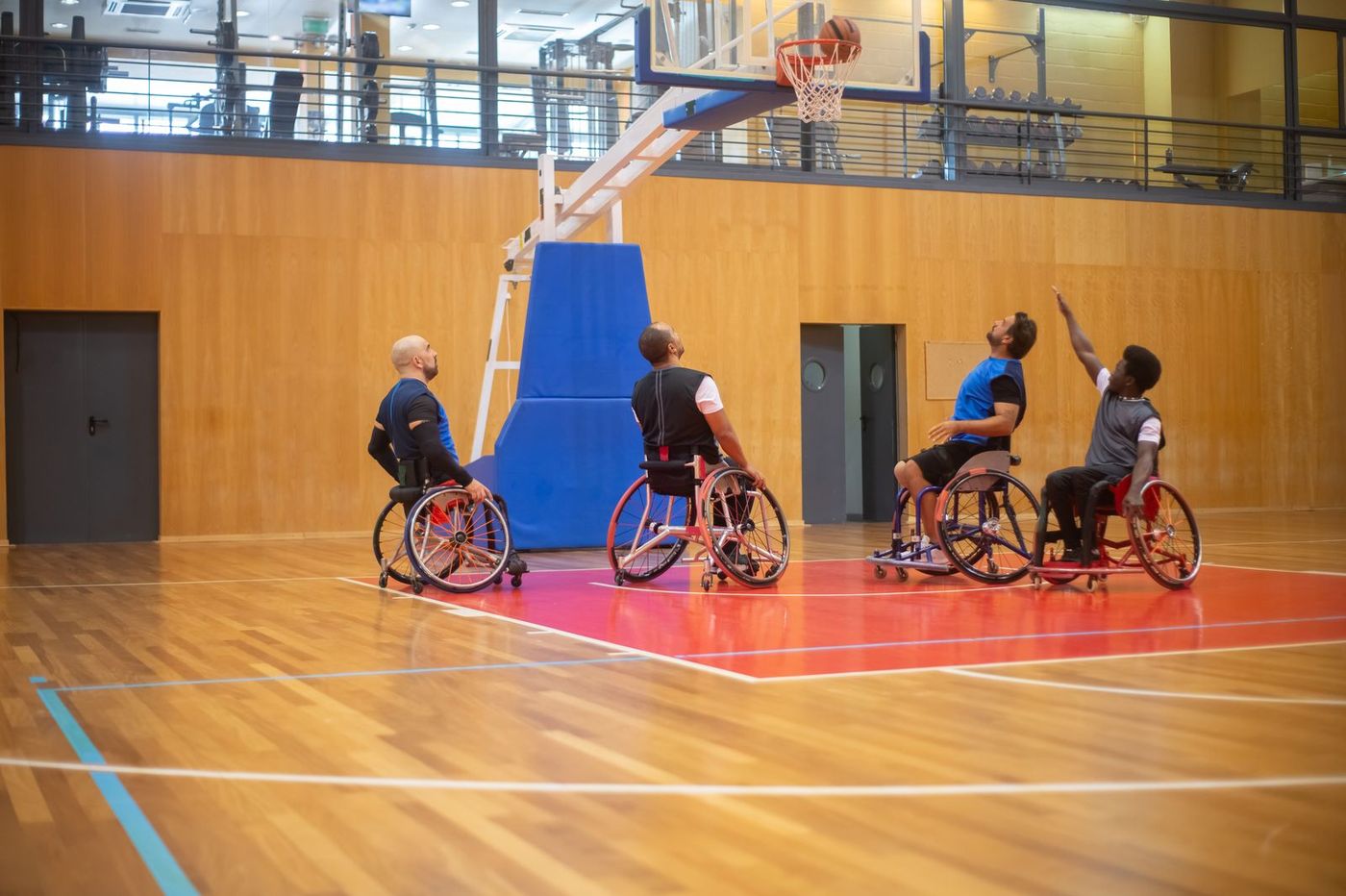 Four wheelchair basketball players on an indoor court watching a shot go through the hoop