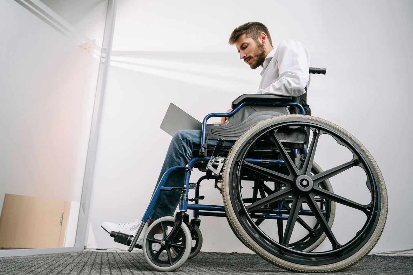 A man seated in a manual wheelchair working on a laptop in a bright office