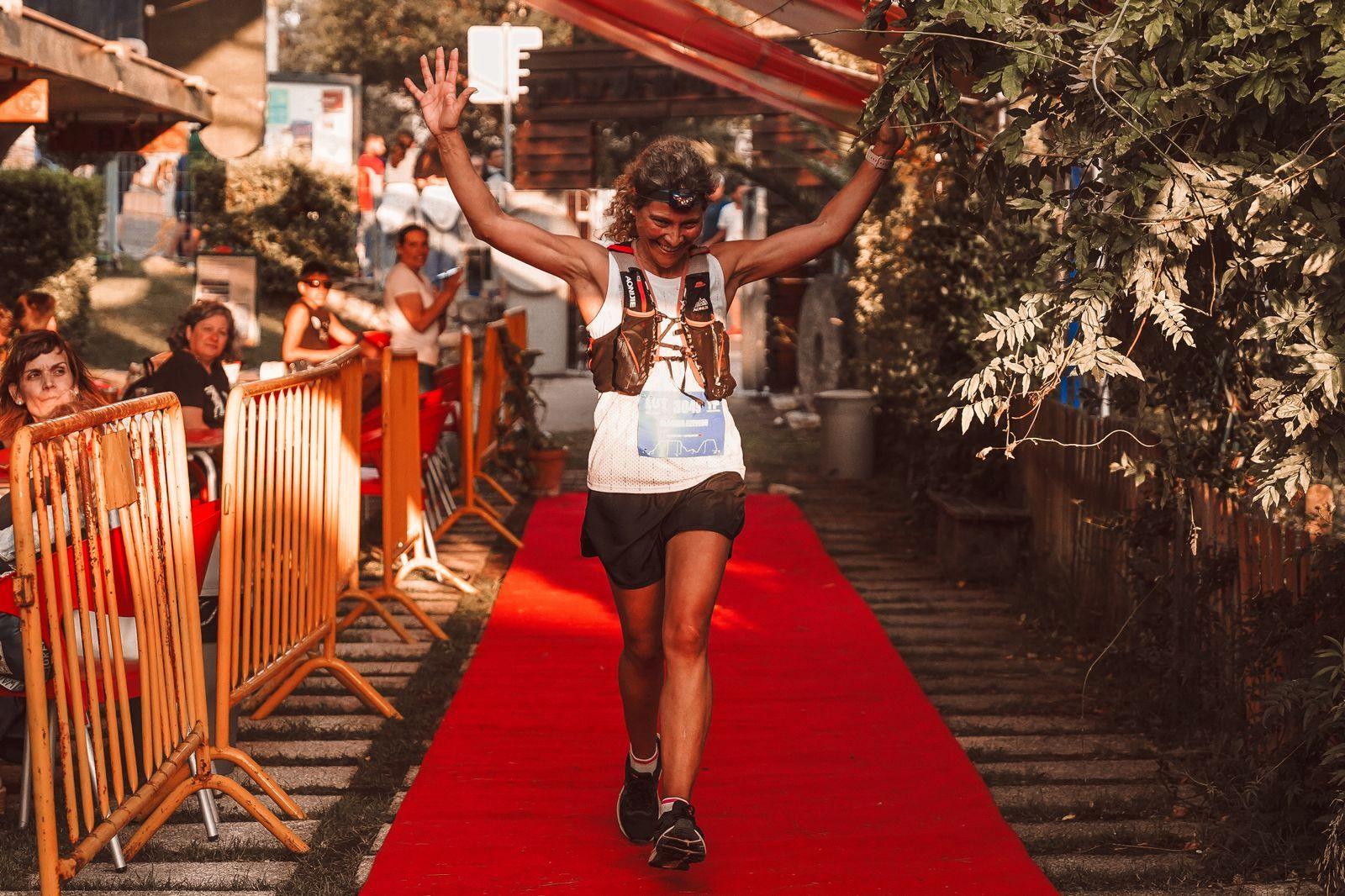 A smiling runner crossing a finish line on a red carpet with both arms raised