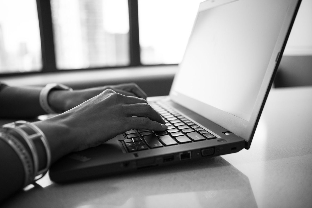 Black and white close up of hands typing on a laptop keyboard
