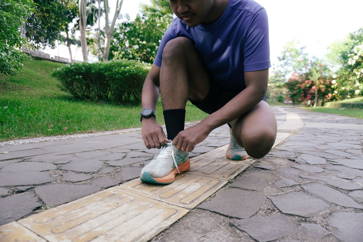 A runner crouches on a park path to tie a shoe before a morning jog